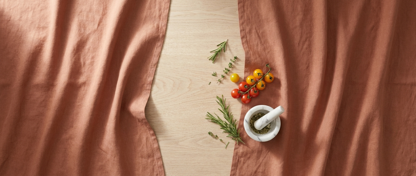 Elegant terracotta linen kitchen flat-lay with marble mortar and pestle, fresh herbs and cherry tomatoes on oak wood table